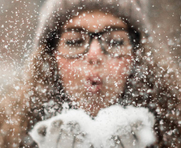 Girl with glasses blowing snow from hear hands